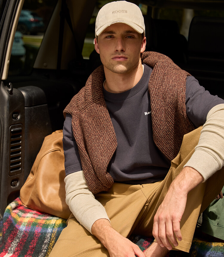 Model wearing a brown knit zip sweater and matching pants beside canoes.