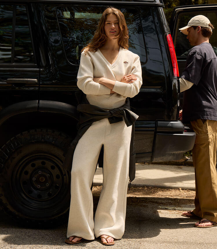 Model wearing a brown knit zip sweater and matching pants beside canoes.