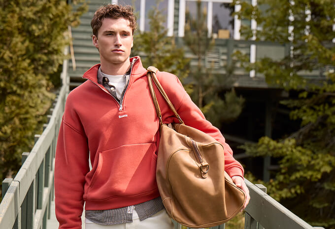 Man wearing a red quarter zip and carrying leather bags.
