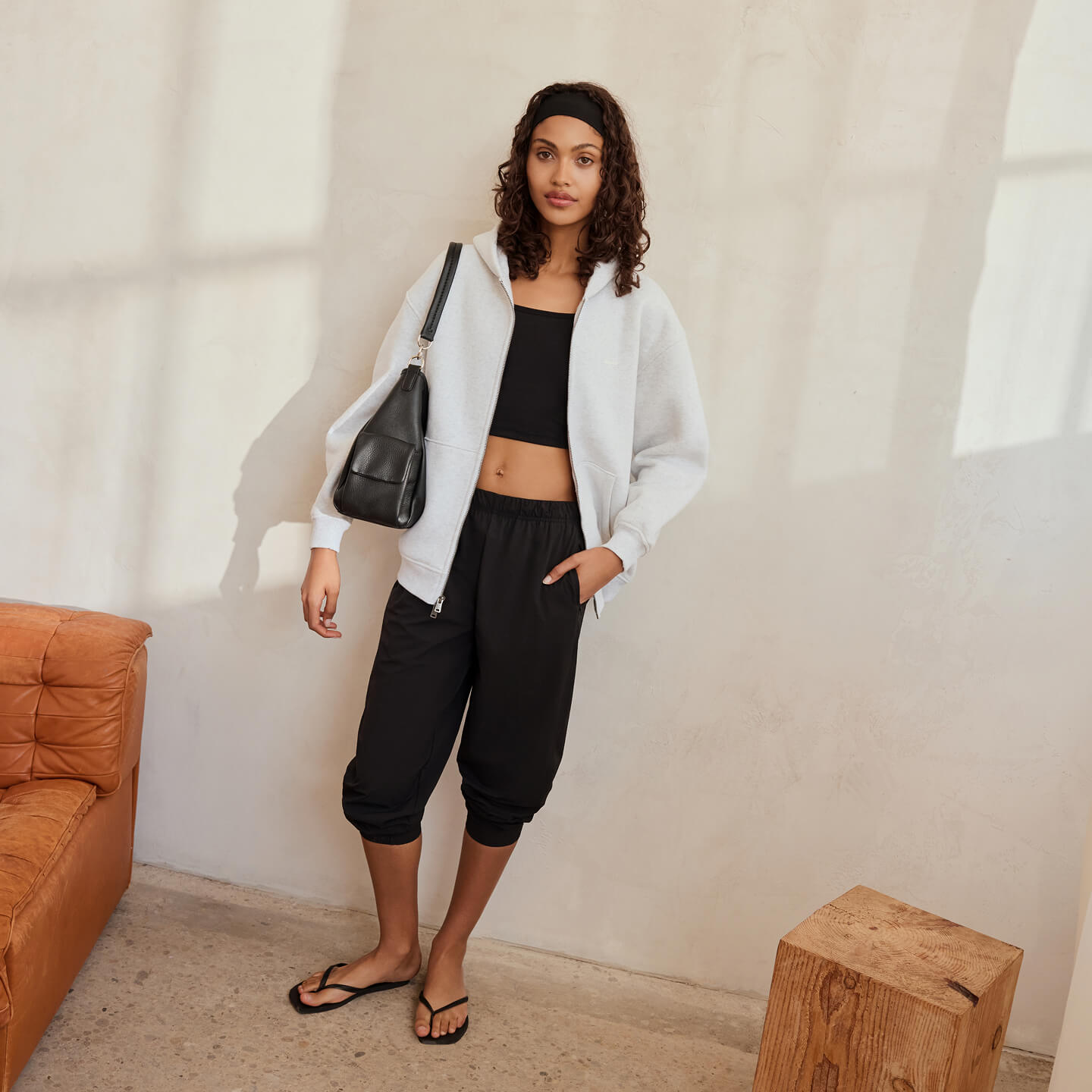 Mannequin portant un kangourou blanc à glissière, un haut court noir, un pantalon jogger noir et des sandales.