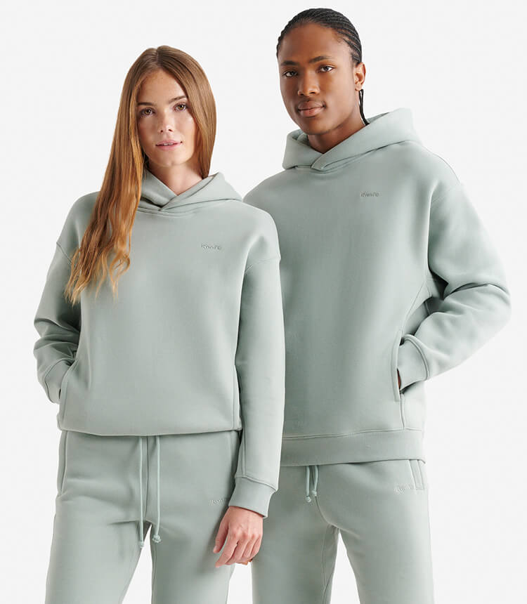 Two models wearing matching gender free sweats in a light sage colour.