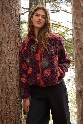 Woman wearing a floral fleece jacket and black pants in the woods.