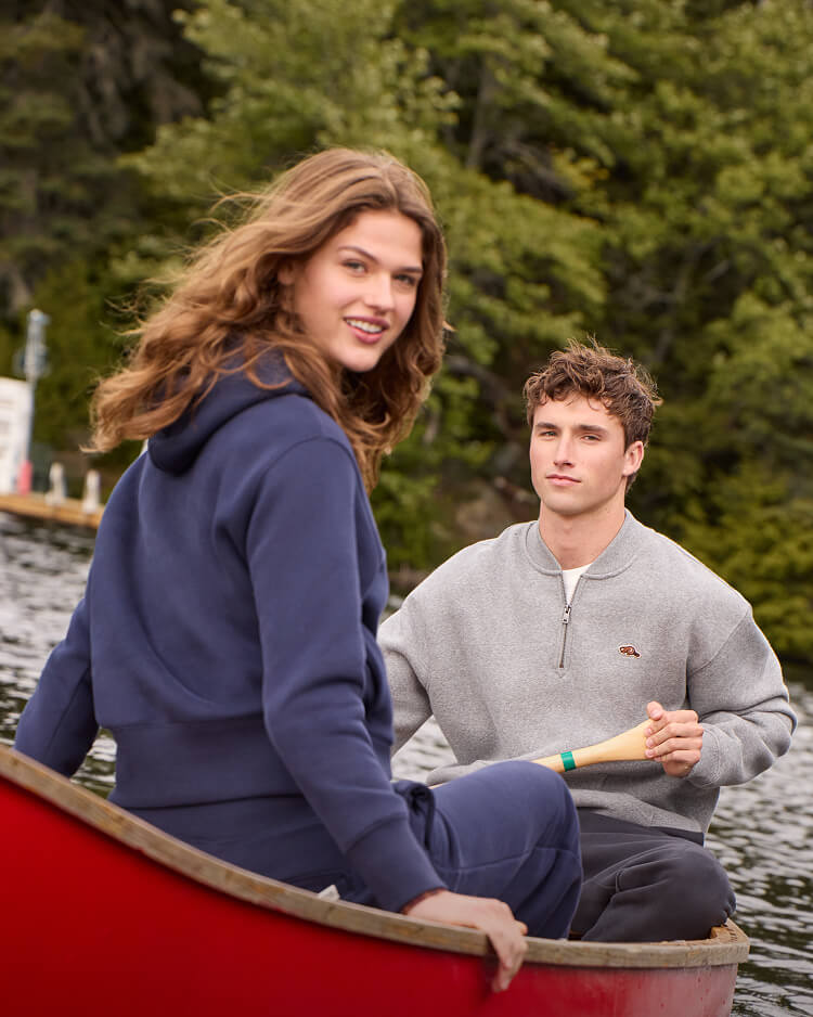 Two models wearing new seasonal Roots styles while canoeing on a lake.