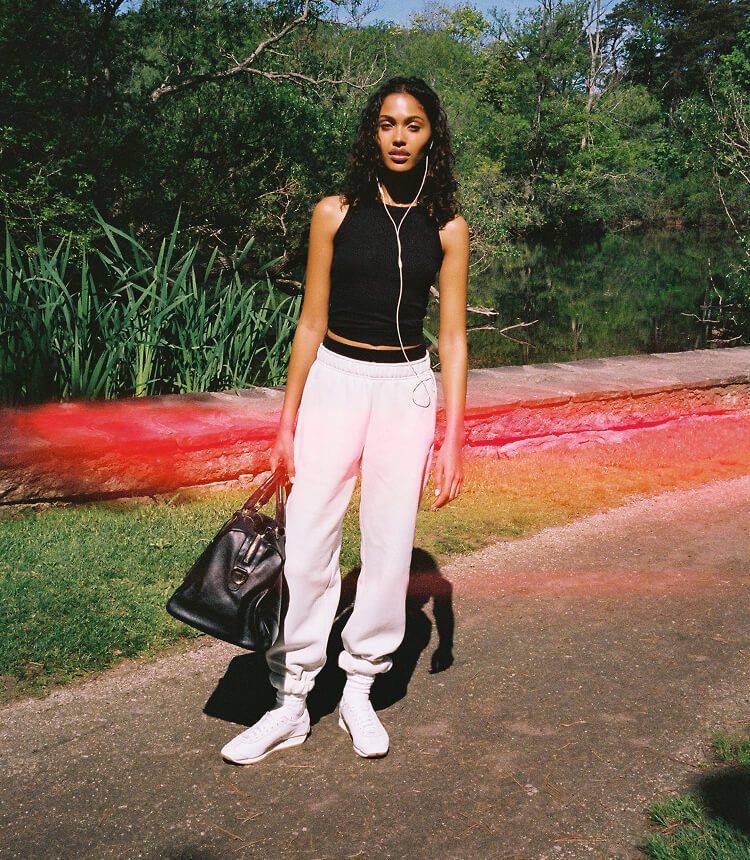 Model wearing a black sleeveless top, light sweatpants, and white sneakers outdoors.